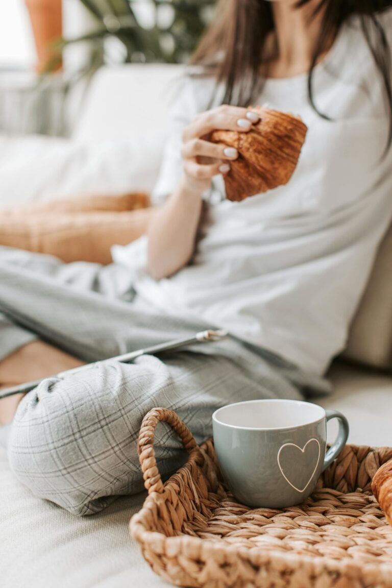 Relaxed morning setting with a woman in pajamas enjoying coffee and pastry indoors.