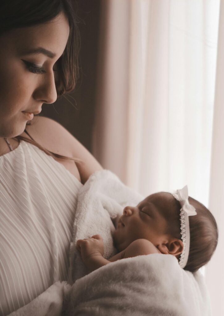 Tender moment of a mother holding her newborn child by a window, capturing love and warmth.