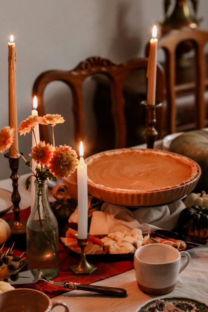 Warm autumn table setting with pumpkin pie, candles, and fall decor, creating a cozy ambiance.